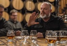 Expert Tips to Decode Any Whiskey Bottle (Without Looking Like a Newbie) A bearded man gestures while explaining whiskey flavors at a tasting event in a barrel room.