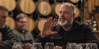 Expert Tips to Decode Any Whiskey Bottle (Without Looking Like a Newbie) A bearded man gestures while explaining whiskey flavors at a tasting event in a barrel room.